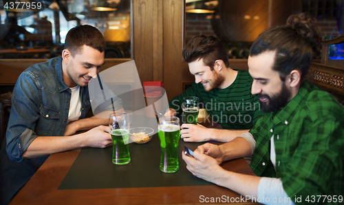 Image of friends with smarphones and green beer at pub