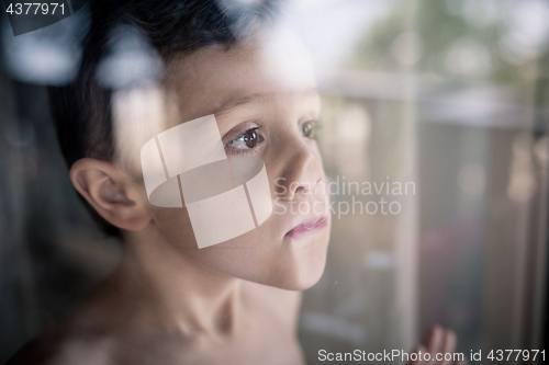 Image of one sad little boy standing near the window at the day time.