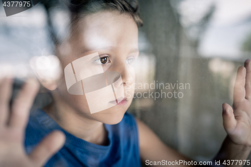 Image of one sad little boy standing near the window at the day time.