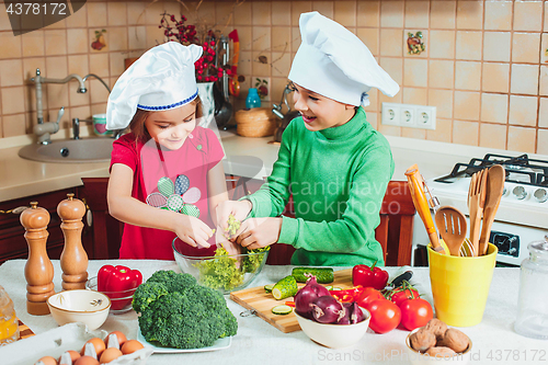 Image of happy family funny kids are preparing the a fresh vegetable salad in the kitchen