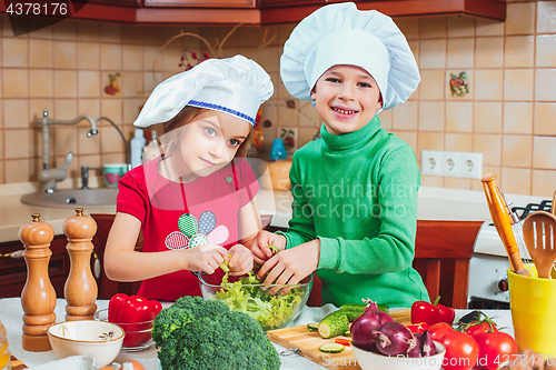 Image of happy family funny kids are preparing the a fresh vegetable salad in the kitchen