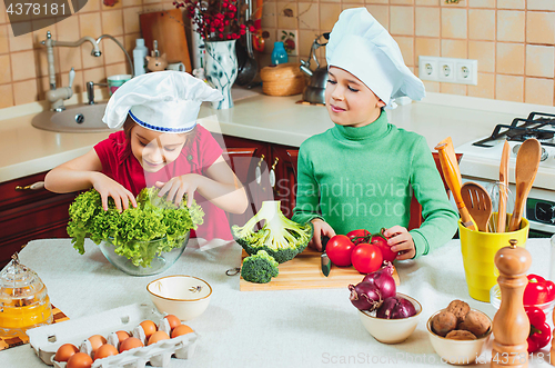 Image of happy family funny kids are preparing the a fresh vegetable salad in the kitchen