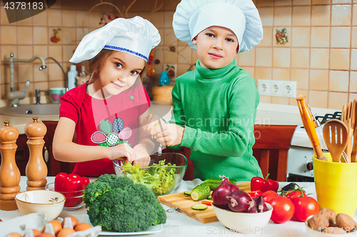 Image of happy family funny kids are preparing the a fresh vegetable salad in the kitchen