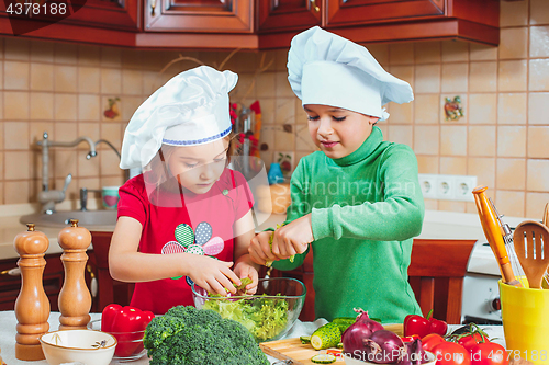 Image of happy family funny kids are preparing the a fresh vegetable salad in the kitchen