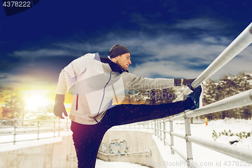 Image of sports man stretching leg at fence in winter