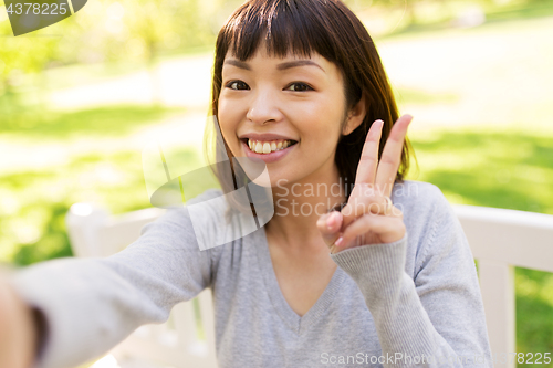 Image of happy asian woman taking selfie and showing peace