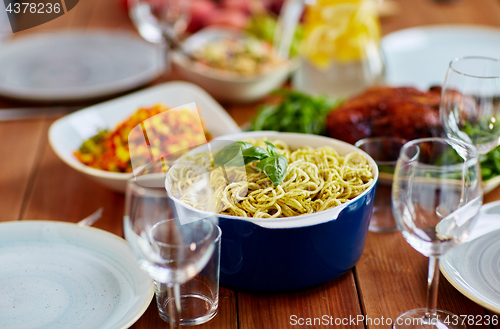 Image of pasta with basil in bowl and other food on table