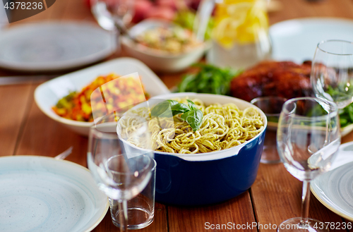 Image of pasta with basil in bowl and other food on table