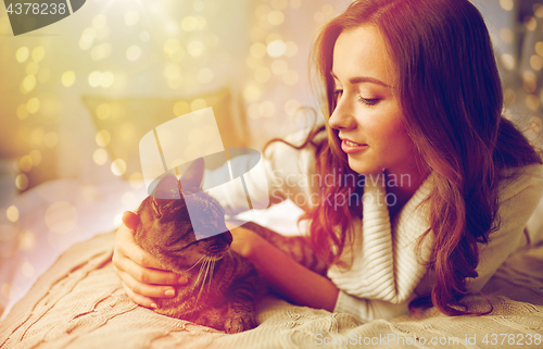 Image of happy young woman with cat lying in bed at home