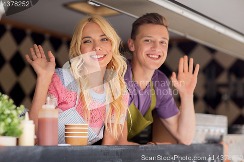 Image of happy young sellers waving hands at food truck