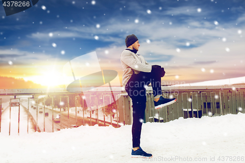 Image of man exercising and stretching leg on winter bridge