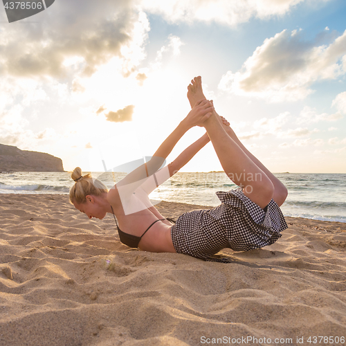 Image of Woman practicing yoga on sea beach at sunset.