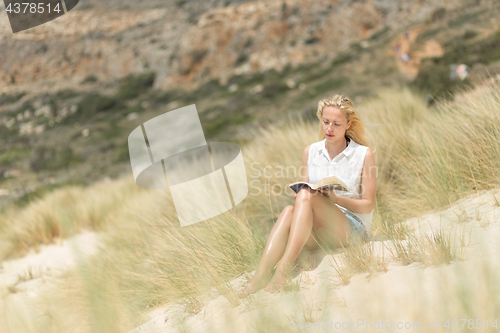 Image of Woman reading book, enjoying sun on beach.