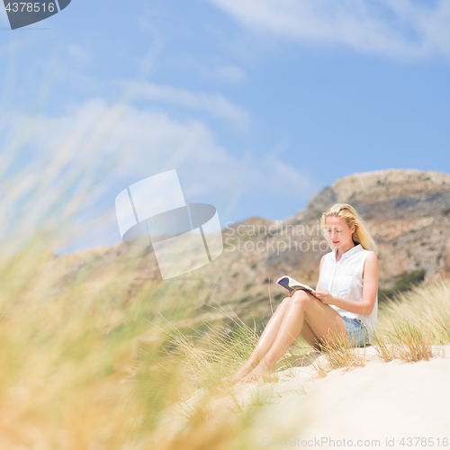 Image of Woman reading book, enjoying sun on beach.