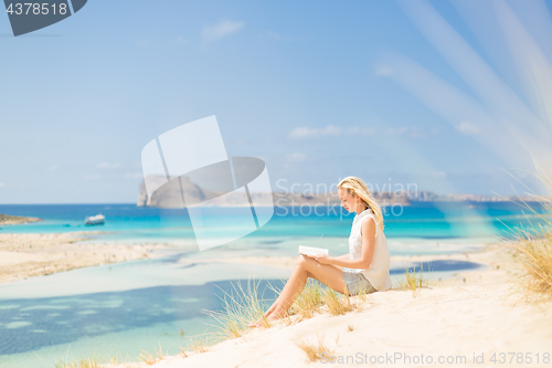 Image of Woman reading book, enjoying sun on beach.