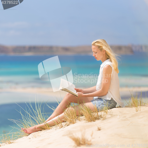 Image of Woman reading book, enjoying sun on beach.