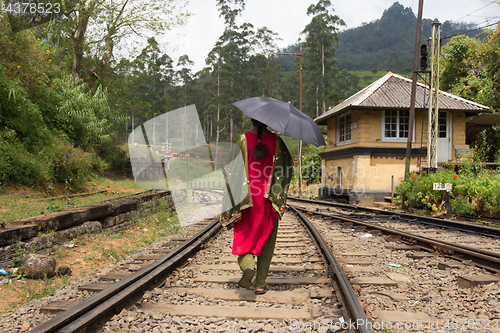 Image of Woman wearing traditional sari and black umbrella walking on railway tracks in Sri Lanka.