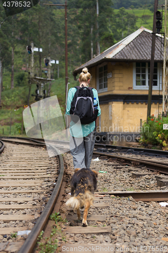 Image of Female backpacker walking on railroad track followed by her dog.