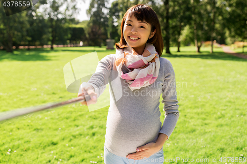 Image of happy pregnant asian woman taking selfie at park