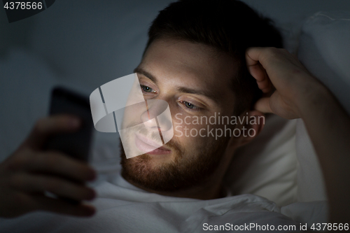 Image of happy young man with smartphone in bed at night