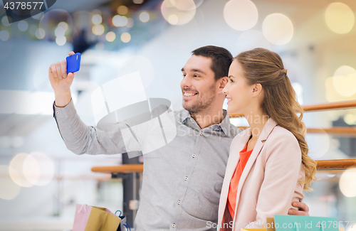 Image of happy couple with smartphone taking selfie in mall