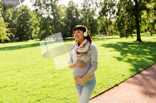 Image of happy pregnant asian woman in headphones at park