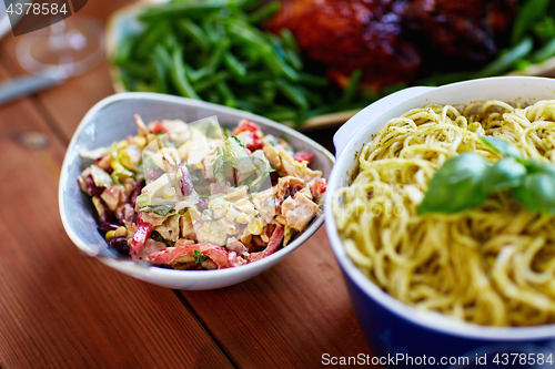 Image of salad and pasta in bowls with other food on table