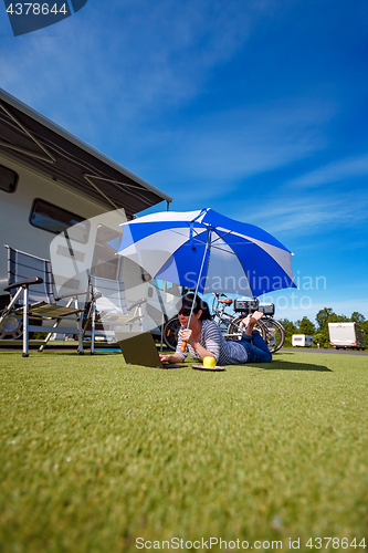 Image of Woman on the grass, looking at the laptop under umbrella near th