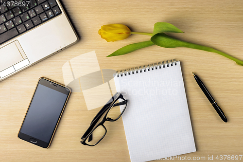 Image of Workspace on the table are tulip, notebook, laptop, glasses, smartphone and pen