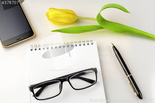 Image of Workspace on table are tulip, notebook, glasses, smartphone and pen