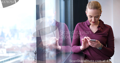 Image of Elegant Woman Using Mobile Phone by window in office building