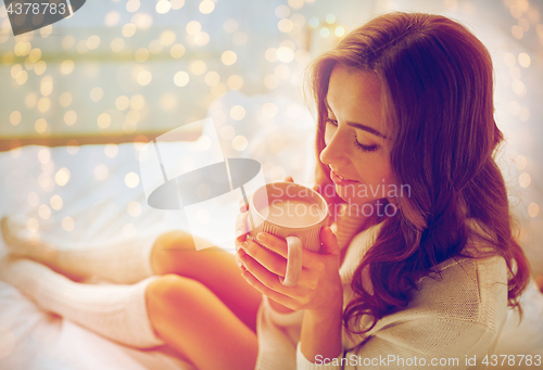 Image of happy woman with cup of cocoa in bed at home