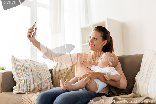 Image of happy mother with baby boy taking selfie at home