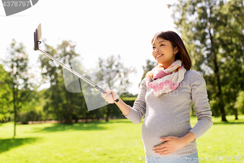 Image of happy pregnant asian woman taking selfie at park