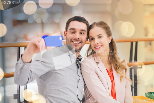 Image of happy couple with smartphone taking selfie in mall