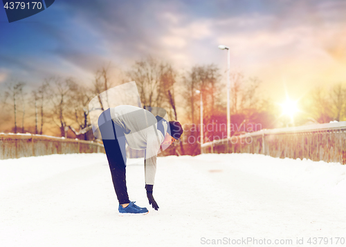 Image of man exercising and stretching leg on winter bridge