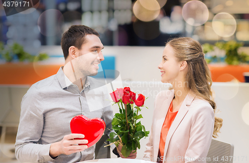 Image of happy couple with present and flowers in mall