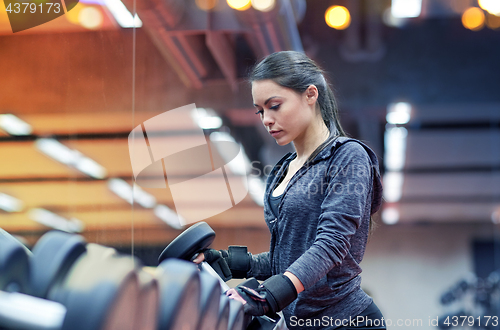 Image of young woman choosing dumbbells in gym