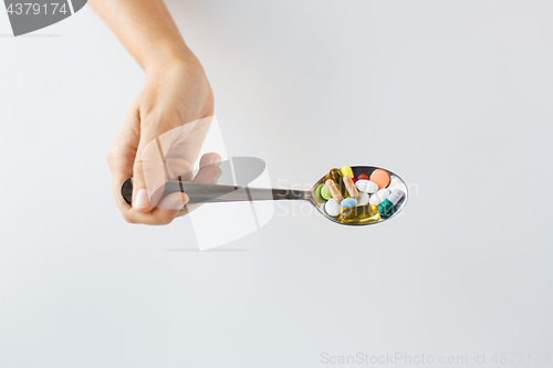 Image of close up of female hand holding spoon with pills