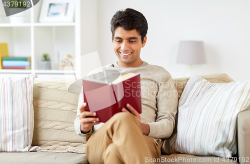 Image of man sitting on sofa and reading book at home