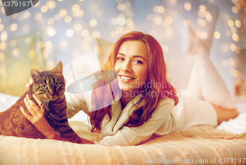 Image of happy young woman with cat lying in bed at home