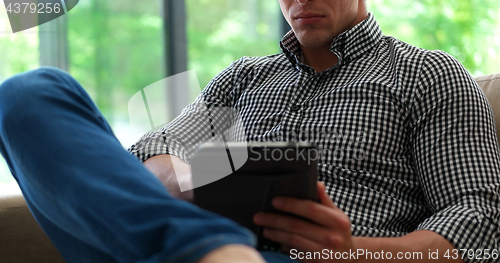 Image of Man is Laying on Couch at Home and Using Tablet