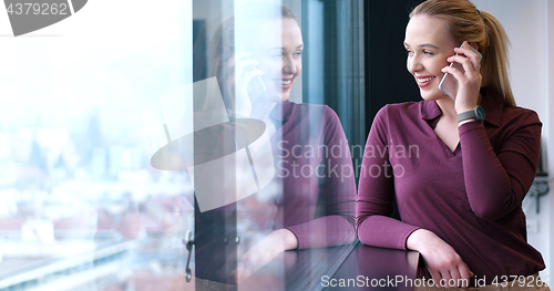 Image of Elegant Woman Using Mobile Phone by window in office building