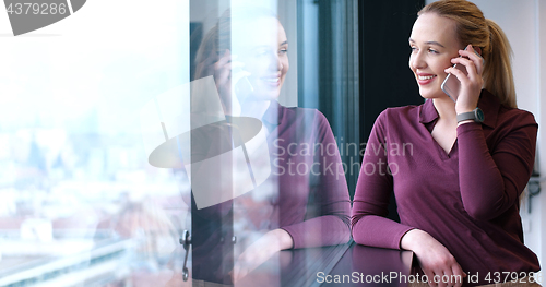 Image of Elegant Woman Using Mobile Phone by window in office building