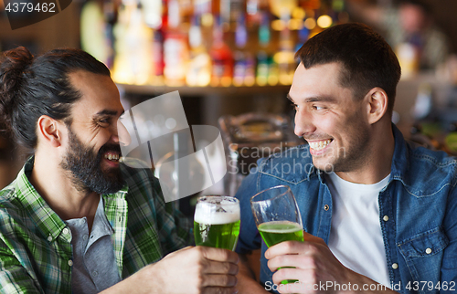 Image of male friends drinking green beer at bar or pub