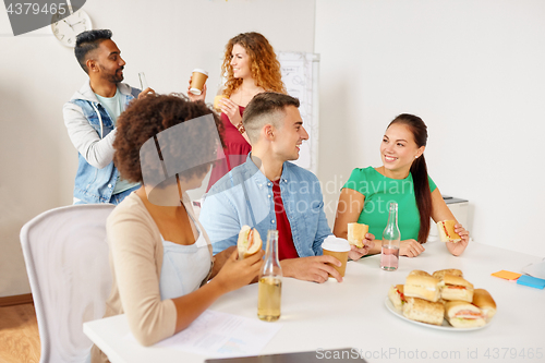 Image of happy friends or team eating at office
