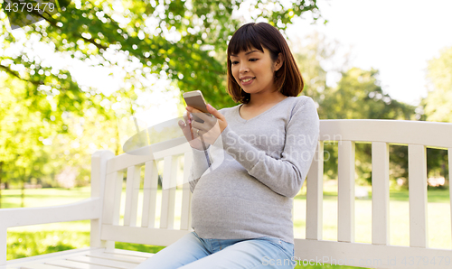 Image of happy pregnant asian woman with smartphone at park