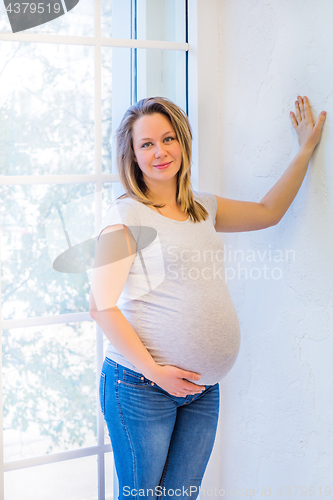 Image of Cute pregnant woman standing near window