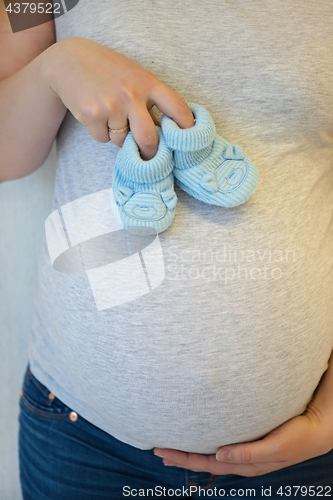 Image of Pregnant woman holding blue baby booties