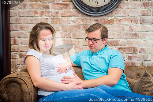 Image of Happy pregnant woman and man sitting near wall